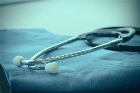 Stethoscope with blue doctor coat on wooden table with shallow DOF evenly matched and background ...