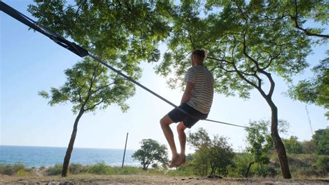 Athlete walking in slackline in the park with sea and blue sky on ...