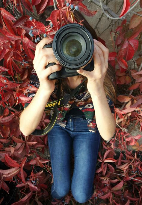 Woman Holding Dslr Camera Sitting on Red Leaved Plant · Free Stock Photo