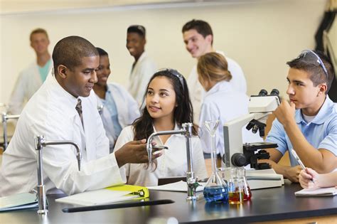 High school science teacher talking with students in chemistry lab - WSPTA