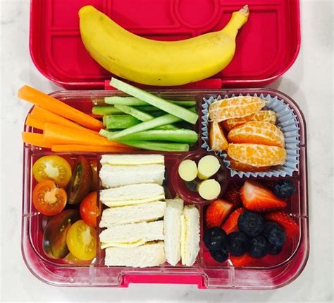 a plastic container filled with fruit and veggies next to a banana on top of a table