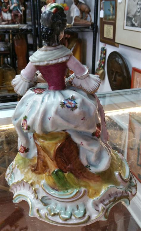 I need some more info on this antique porcelain figurine. It depicts a woman in a dress seated ...