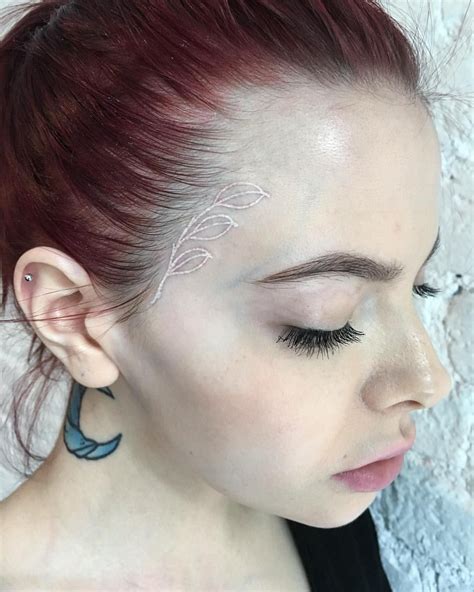 a woman with red hair has tattoos on her face and behind her ear is a ...