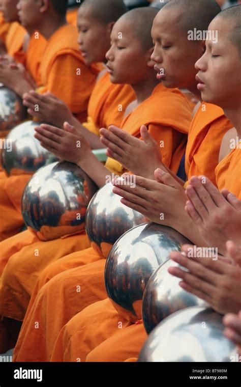 Buddhist monks wearing orange robes are praying with their alms bowls near Tha Pae Gate in ...