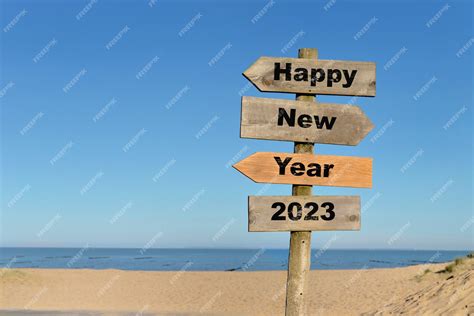 Premium Photo | 2023 happy new year written on a direction sign in front of a beach on blue sky