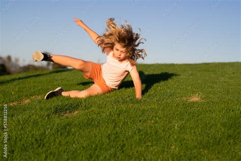 Kid runs through the spring grass and falling down on the ground in park. Moment of the fall ...