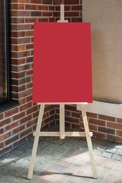 Premium Photo | Wooden artist easel with red blank mockup poster for your design in front of ...