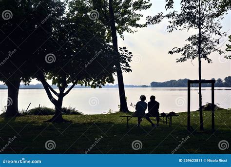 Couple Sitting on a Bench by the Lakeshore at Sunset Seen from the Distance Stock Image - Image ...