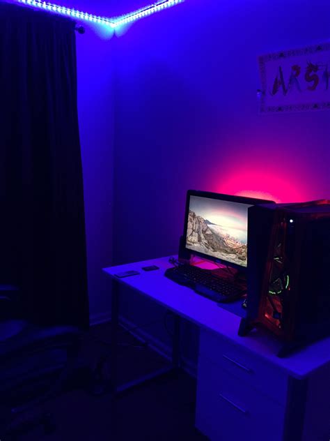 a computer desk with a monitor and keyboard on it in a room lit by purple lights