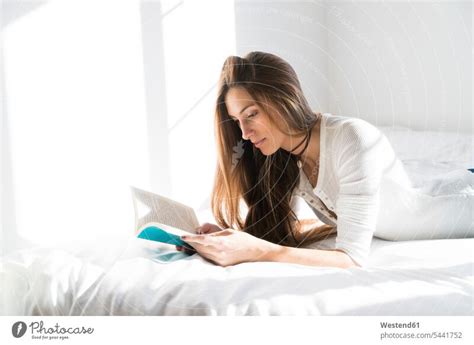 Young woman lying on bed reading book - a Royalty Free Stock Photo from Photocase