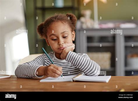 Front view portrait of cute African-American girl drawing while sitting at wooden desk, copy ...