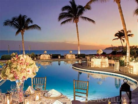 an outdoor dining area next to a swimming pool at dusk with candles and flowers on the table