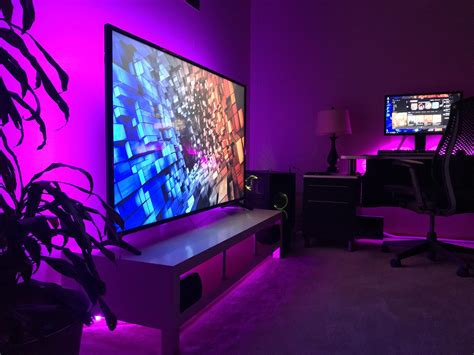 a living room with purple lighting and two monitors on the wall in front of it