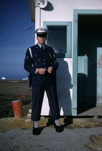 a man in uniform standing next to a white building with a blue door and window