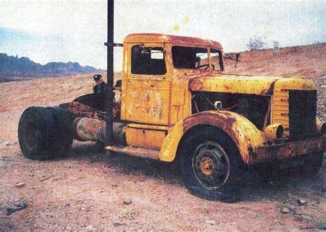 an old yellow truck is parked in the dirt near a light pole and some rocks