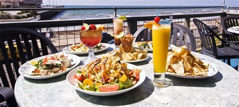 plates of food and drinks sit on an outdoor table overlooking the ocean ...