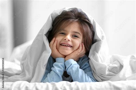 Cute little girl lying on bed under blanket Stock Photo | Adobe Stock