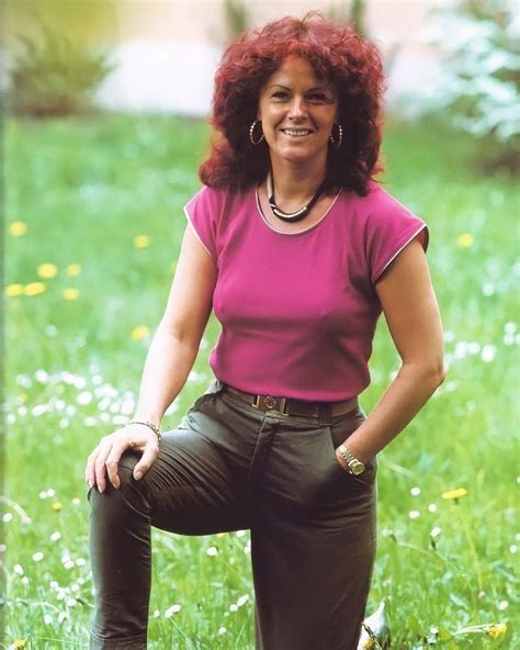 a woman with red hair is sitting in the grass and smiling at the camera while wearing green pants