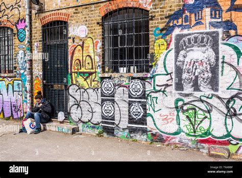 Woman sitting in front of graffiti in the famous Shoreditch Graffiti Wall at Seven Stars Yard, a ...