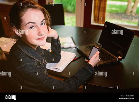 Teenaged girl is studying at the family kitchen table and researches something on her phone ...