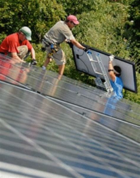 three men working on the roof of a house with solar panels and trees in the background
