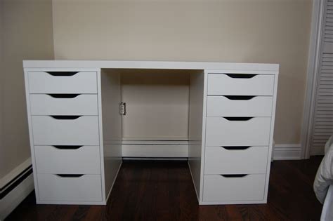 a white desk with black drawers in a room next to a wall and hardwood floor