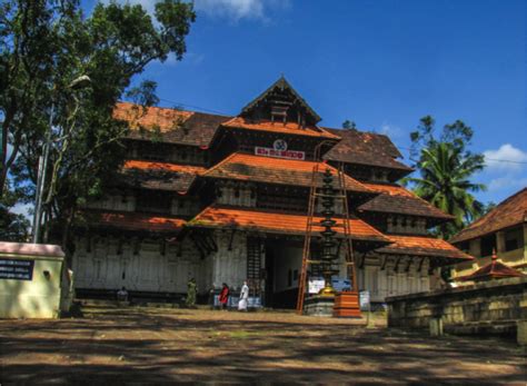 an old wooden building sitting in the middle of a park with people standing around it