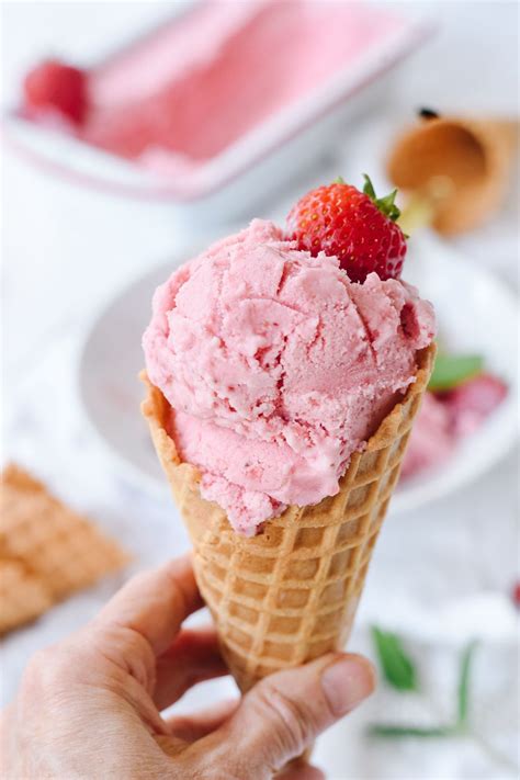 a hand holding an ice cream cone with strawberries on top