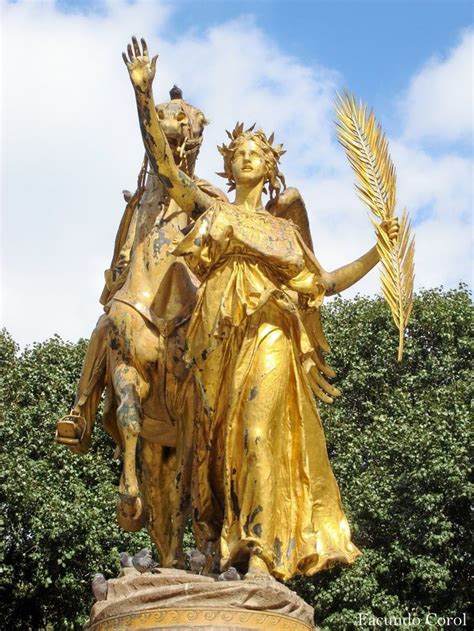 a golden statue holding a plant in it's hand and standing next to a tree