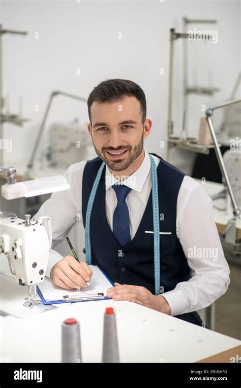 Male tailor sitting at sewing machine, making notes, smiling Stock ...