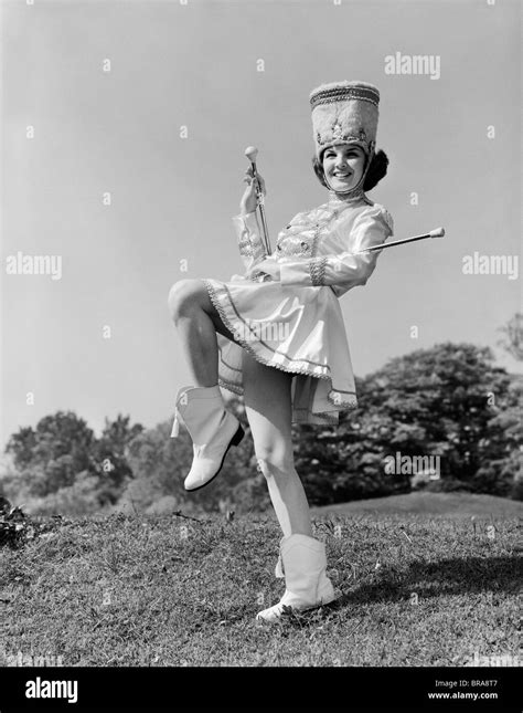 1960s SMILING MAJORETTE IN UNIFORM WITH SHORT SKIRT BOOTS TALL HAT AND TWO BATONS POSING ...