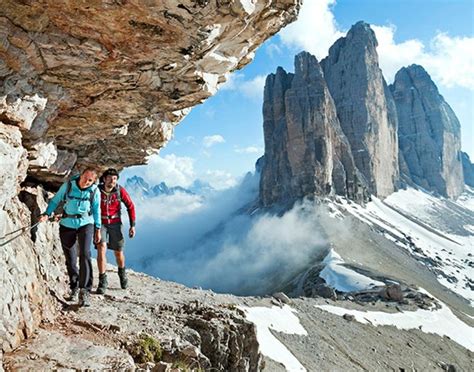 two people hiking up the side of a mountain with snow and clouds in the ...