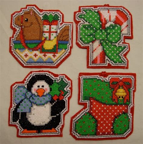 four cross stitch christmas coasters on a white tablecloth with snowman, penguin and reindeer