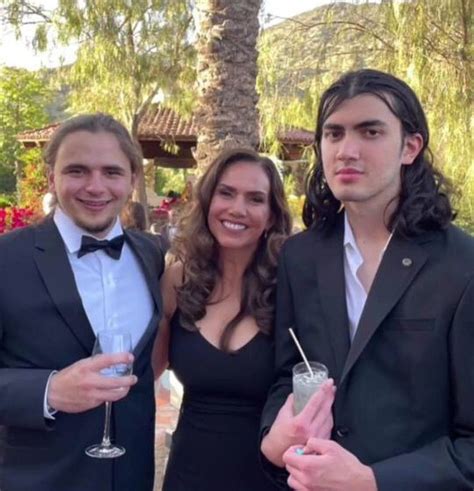 two men and a woman standing next to each other with drinks in front of them