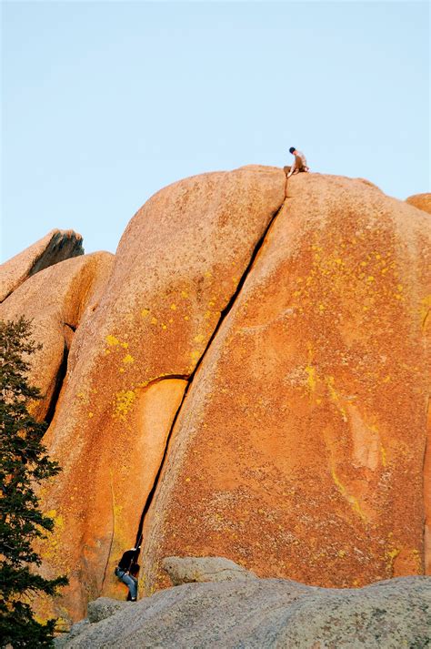 two people are climbing up the side of a large rock with yellow lichen ...