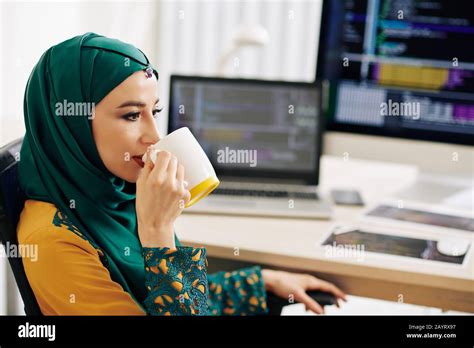 Beautiful young muslim woman in hijab sitting at office table and drinking mug of coffee Stock ...