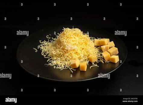 Pile of thin grated gouda cheese on a black ceramic plate, isolated on ...