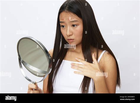 Femme asiatique avec miroir dans la main problèmes de peau faciale, acné et inflammation ...
