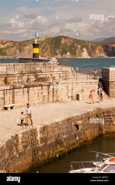 People walking on the harbour in front of the lighthouse at Comillas ...