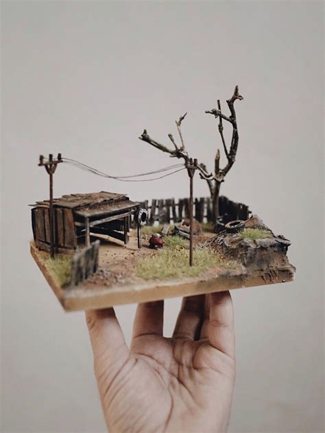 a hand holding up a miniature model of a house and tree in front of a white wall