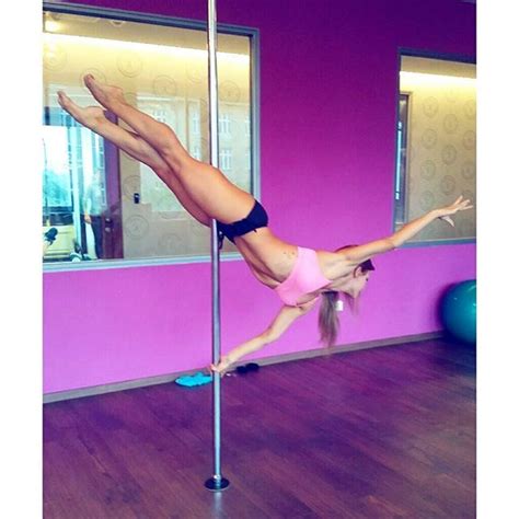 a woman is doing tricks on a pole in a room with pink walls and wood floors