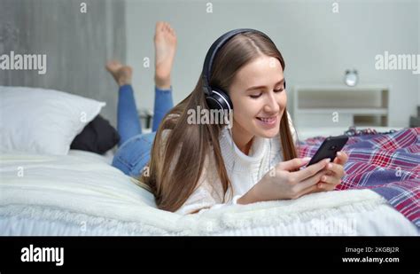 Barefoot young pretty girl lying on bed in bedroom listening music using Stock Video Footage - Alamy