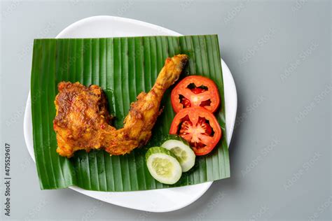 Ayam bakar or roasted chicken on banana leaf shoot at a rustic wooden background. Ayam bakar is ...