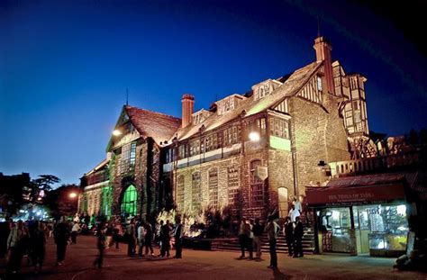 people are walking around in front of an old building at night with the lights on