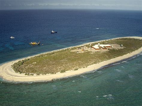 an island in the middle of the ocean with boats floating on it's sides