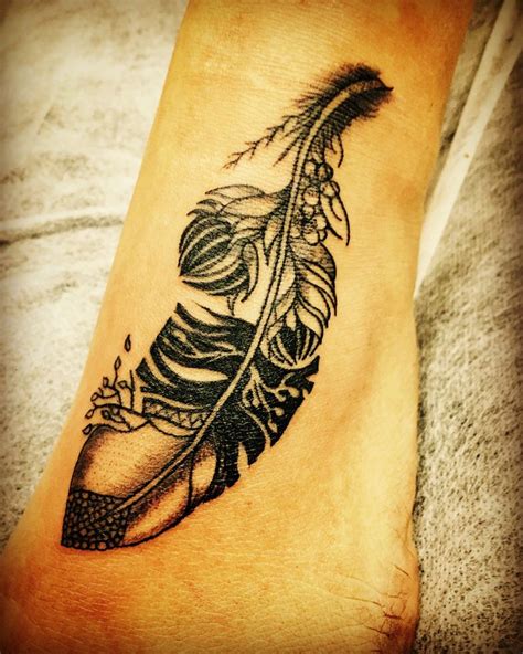 a black and white feather tattoo on the foot with an arrow in it's center
