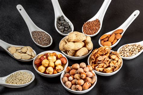 Assortment of nuts and seeds in white bowls and spoons on a black background, close- up ...