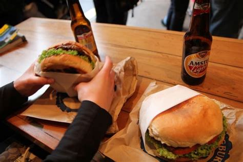 a person holding a sandwich in their hand next to two beer bottles on a table