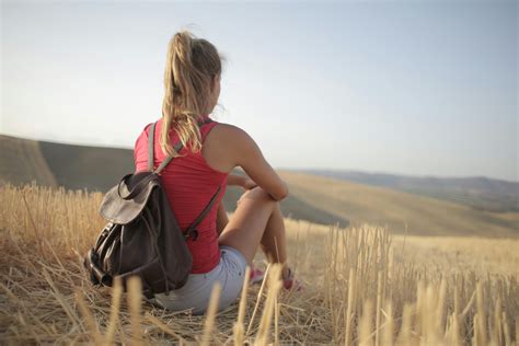 Woman With Leather Backpack While Sitting on Brown Grass Field · Free Stock Photo