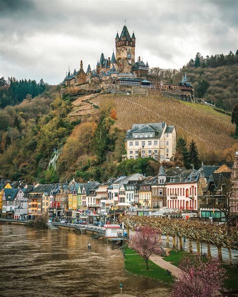 an old castle sits on top of a hill next to a river with boats in it